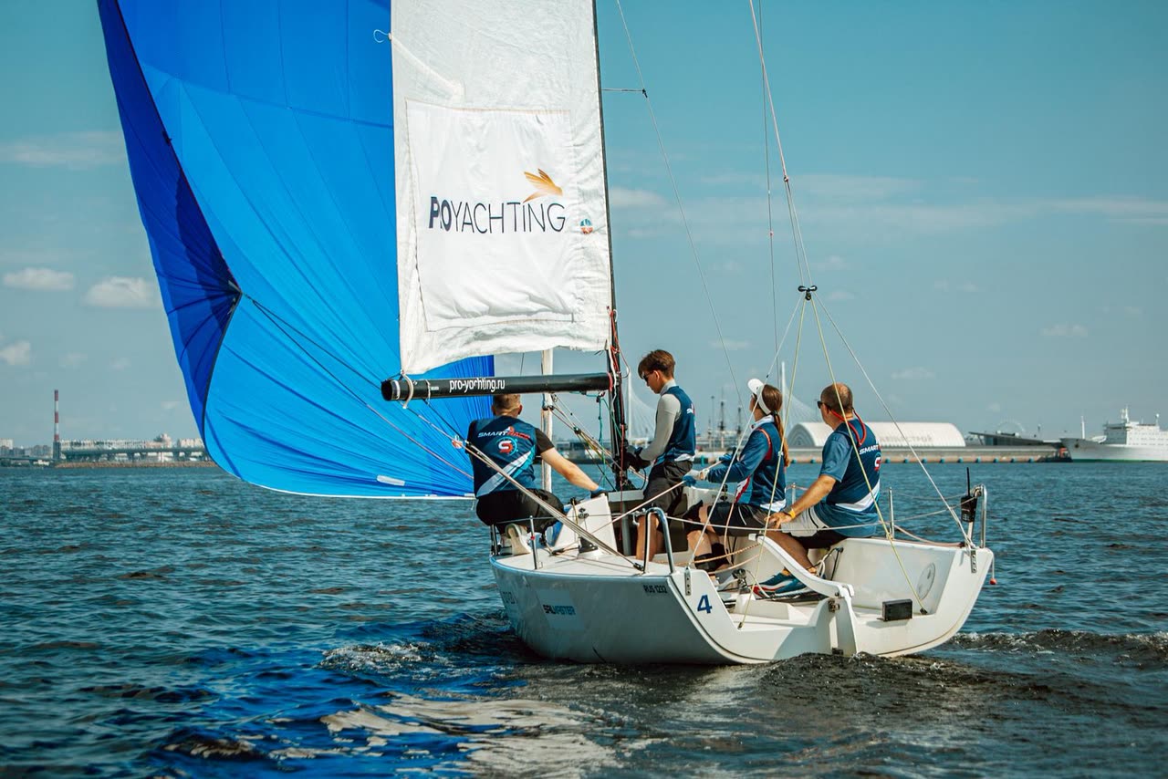 J/70 Smart Race №4 под синим спинакером, за кормой — портовый берег и белый лайнер